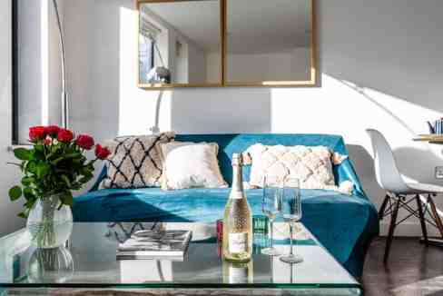 Bright living room with blue sofa, flowers, and sunlight.