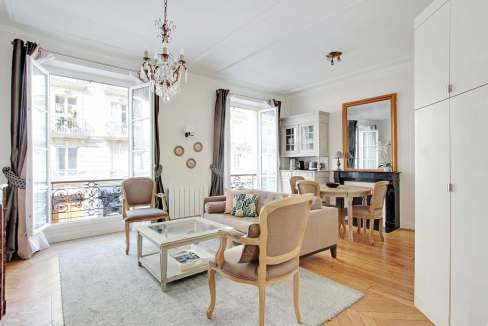 Bright living room with large windows, classic furniture, and chandelier in Paris apartment.