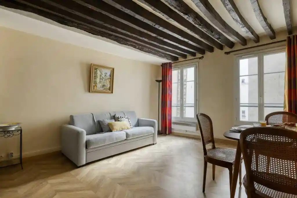 Modern living room with wooden ceiling beams, large windows, and cozy furniture.