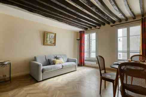 Modern living room with wooden ceiling beams, large windows, and cozy furniture.