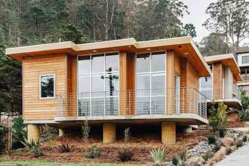 Contemporary wooden cabin with expansive glass windows and balcony in a natural setting.