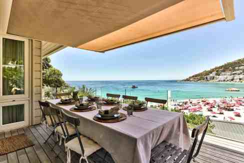 Seaside dining table with ocean view, outdoor terrace, and pink umbrellas on the beach.