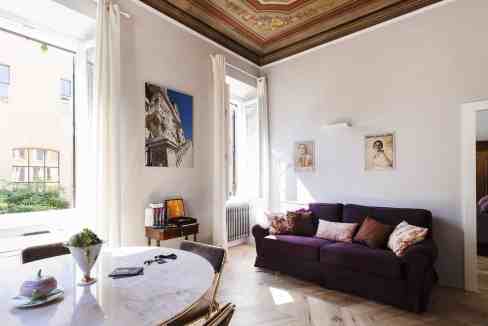 Elegant living room featuring a purple sofa, artwork, and natural light from large windows.