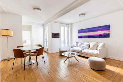 Spacious living room with white walls, wooden floors, a comfortable sofa, and colorful artwork for a.