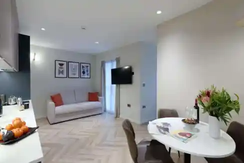 Bright living room with sofa, dining area, and wall-mounted TV in a serviced apartment.