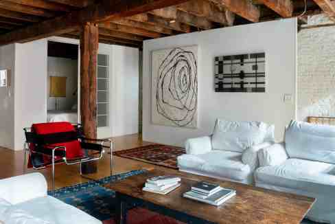 Spacious living room with white sofas, wooden beams, and contemporary artwork.
