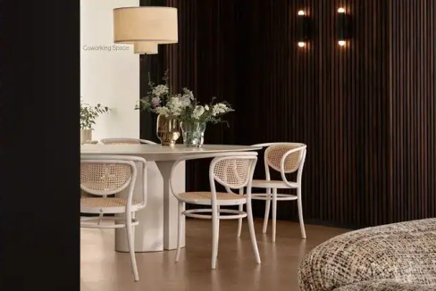 Contemporary coworking area with white table and chairs, cozy lighting, and wooden wall decor.