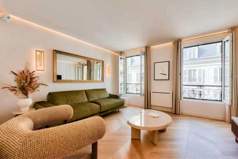 Bright living room with large windows, green sofa, and stylish decor in a serviced apartment.