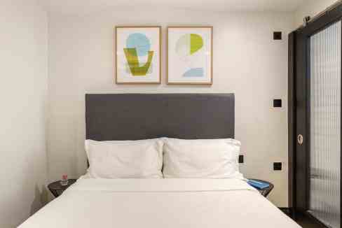Modern bedroom with grey headboard and abstract art.