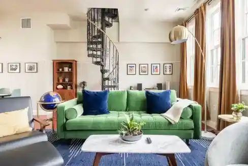 Modern living room with green sofa, spiral staircase, and large windows.