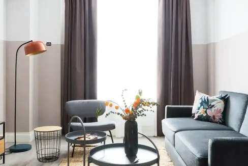 Stylish living room with sofa, armchair, TV, and large window with curtains.