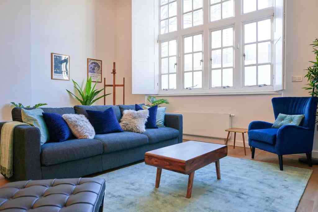 Spacious living room with large windows, blue sofa, and modern decor in Hoxton Loft.