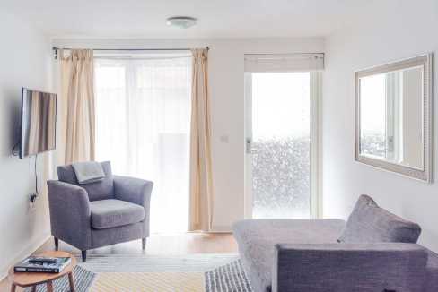Bright living room with large window, gray sofa, armchair, and wall-mounted TV.