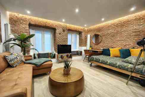 Modern living room with exposed brick walls, large windows, and cozy seating.