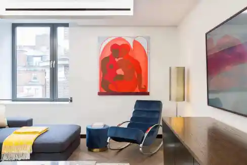 Contemporary living room with artwork, blue chair, and window view.