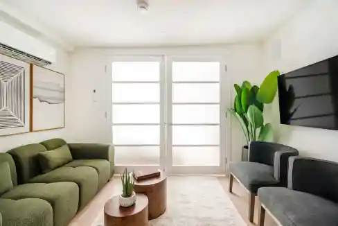 Bright living room with green and gray sofas, large windows, and modern decor.