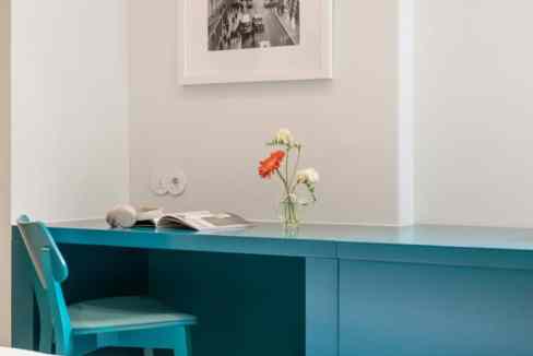 Modern blue desk with a chair and a vase of flowers in a bright room.