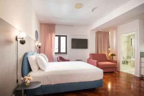 Modern hotel room with a large bed, pink sofa, and flat-screen TV in Lisbon.