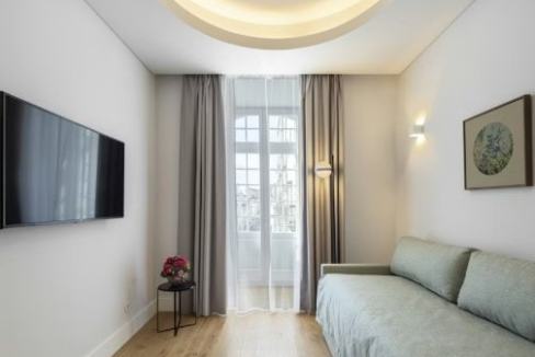 Modern living room with large window, sofa, and wall-mounted TV in Lisbon.