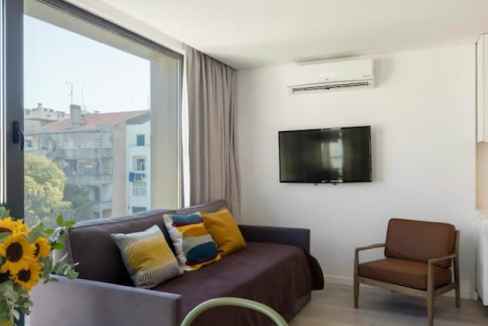 Modern serviced apartment living room with large window and city view.