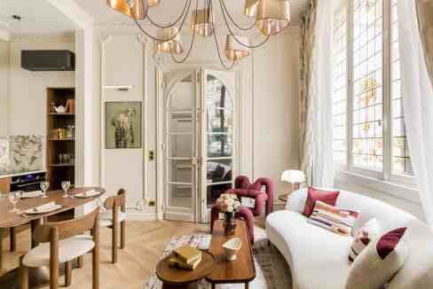 Stylish living room with white sofa, pink armchair, and large windows.