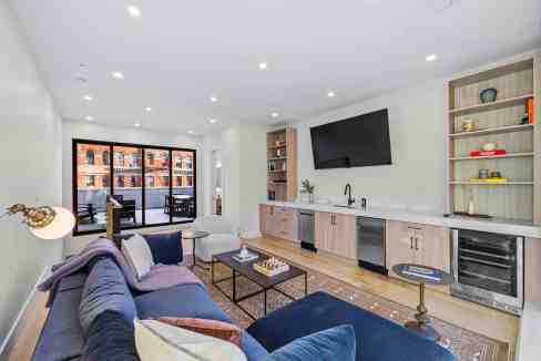 Contemporary living room with sofa, TV, and open kitchen in Harlem Terrace Brownstone.