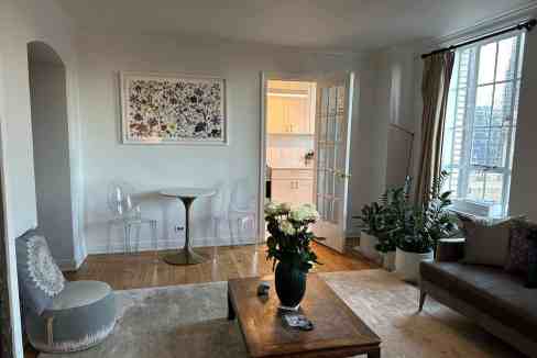 Sunny living room with large windows and garden view, modern furniture, and indoor plants.