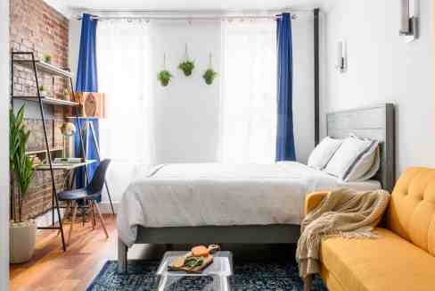 Bright bedroom with white walls, blue curtains, and a yellow sofa.