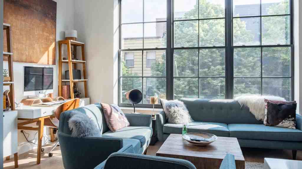 Bright living room with large windows, blue sofas, and cozy cushions.