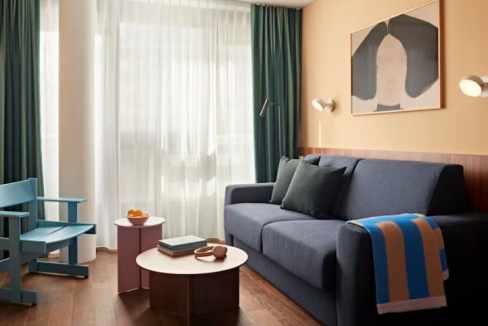 Modern living room with blue sofa, armchair, and abstract wall art in Stuttgart Mitte Suites.