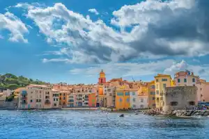 Colorful buildings along the waterfront in Saint-Tropez under a partly cloudy sky.