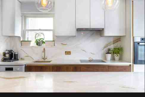 Contemporary kitchen with white cabinets, marble backsplash, and wooden accents.