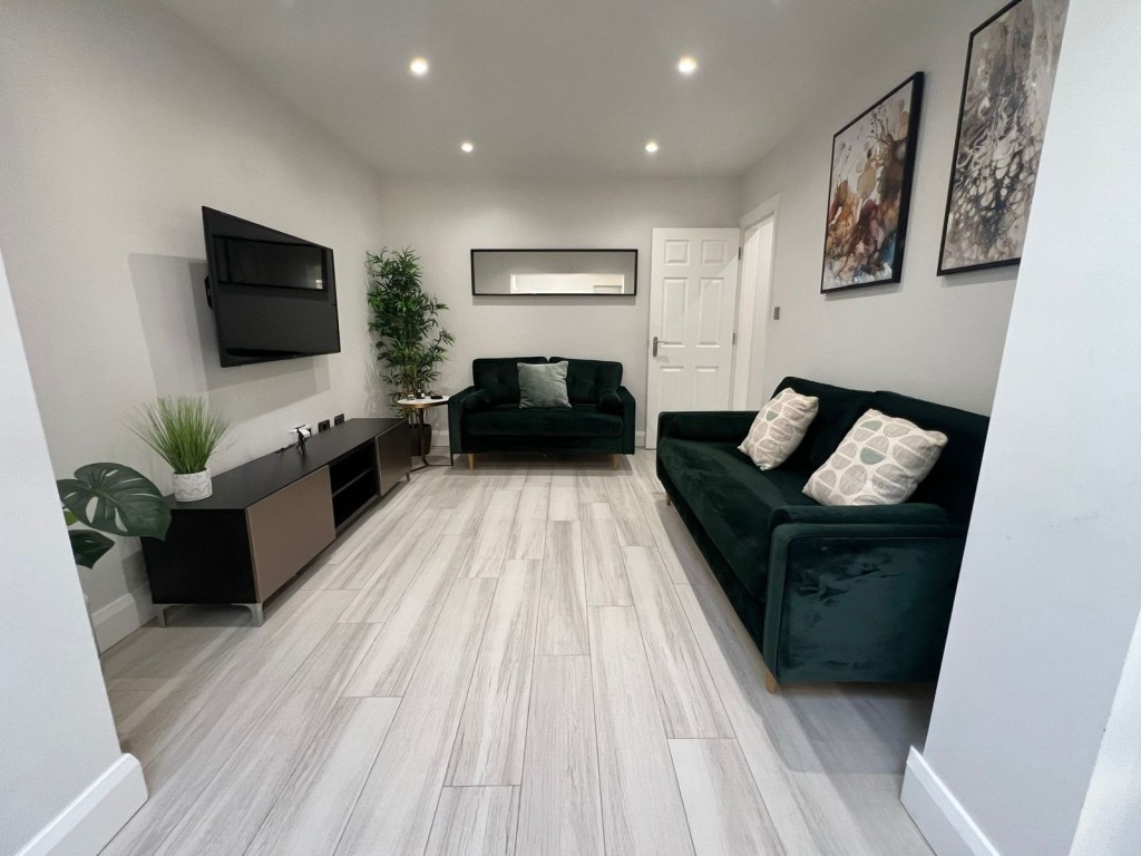 A modern living room in the Harrow Garden Townhouse with two dark green sofas, a wall-mounted TV, framed artwork, and light wood flooring.