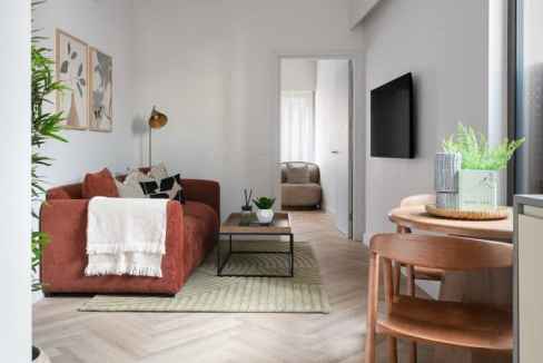 Bright living room with sofa, wall-mounted TV, and dining area in a serviced apartment.