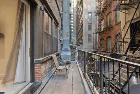 Urban city balcony with chairs overlooking neighboring buildings.