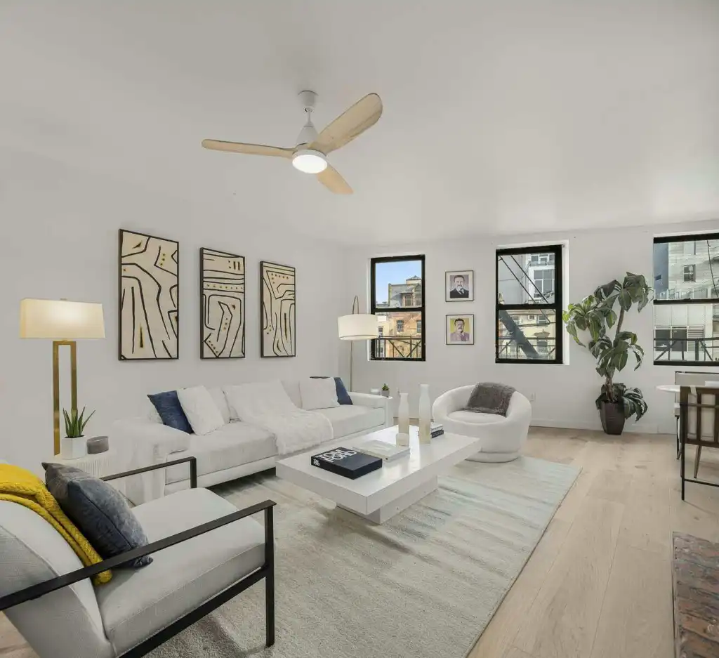 Bright, stylish living room with white furniture, artwork, and large windows in NoHo Brick Poise.