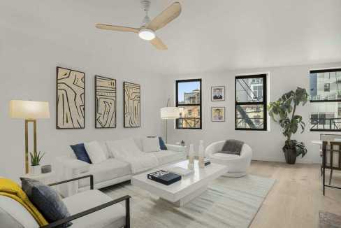 Bright, stylish living room with white furniture, artwork, and large windows in NoHo Brick Poise.