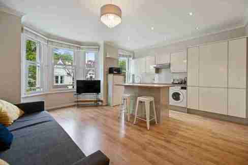 Spacious living room with large bay windows and open-plan kitchen in London.