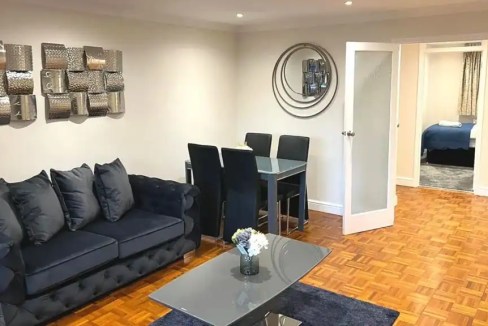 Modern living room with dark sofa, dining area, and bedroom in background.