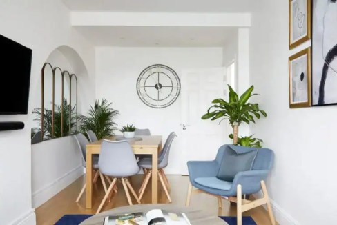 Bright living room with blue armchair, dining table, and green plants.