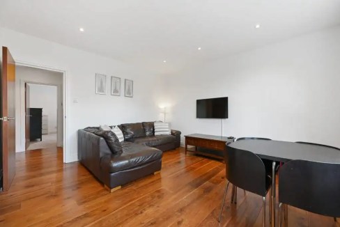Spacious living room with leather sofa, wall-mounted TV, and dining area in Ealing Heritage Luxe.