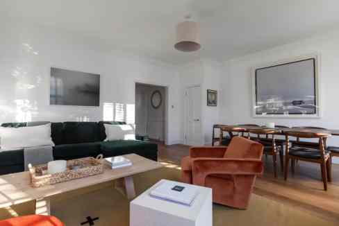 Modern living room with white walls, black sofa, and wooden dining table.