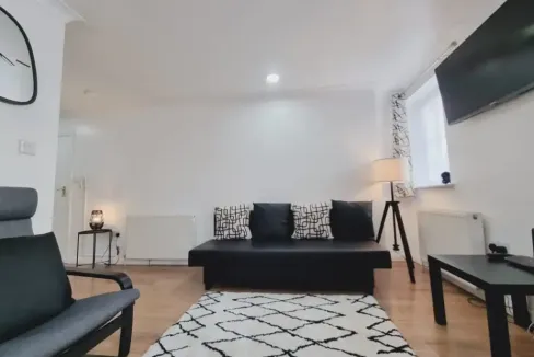 Spacious living room with black sofa, armchair, and flat-screen TV.