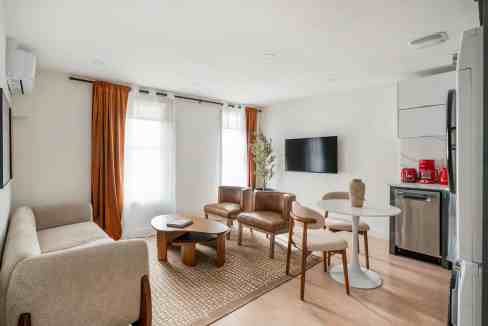 Bright living room with sofa, armchairs, and a wall-mounted TV in a serviced apartment.