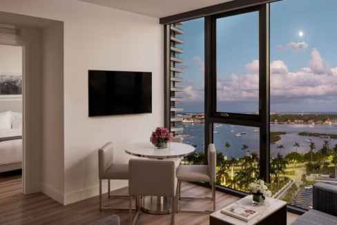 Modern serviced apartment with large windows overlooking river and cityscape.