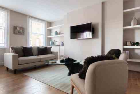 Bright living room with sofa, armchair, TV, and shelves in a serviced apartment.