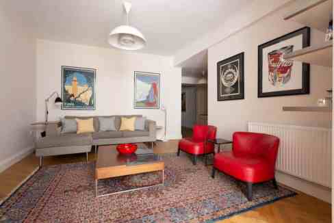Modern living room with grey sofa, red chairs, and artwork in Nordic Notting Hill.
