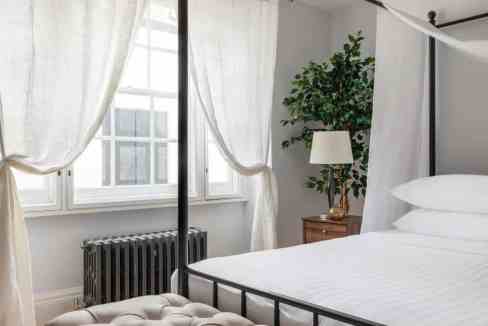 Bright bedroom with large windows, white curtains, and a stylish bed.