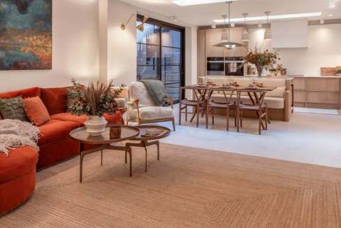 Stylish living room with red sofa, modern decor, and open kitchen in Chelsea townhouse.