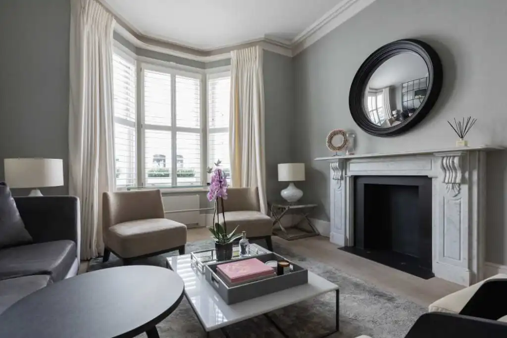 Bright living room with large bay window, modern furniture, and fireplace in Fulham Grand Townhouse.